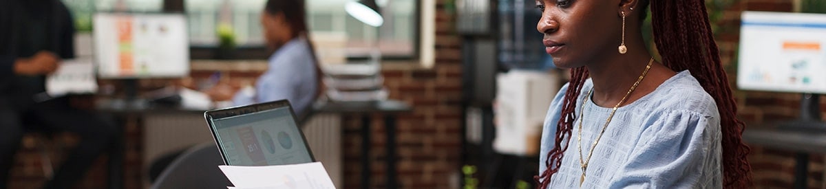 A woman sits at a desk in an office, reviewing paperwork