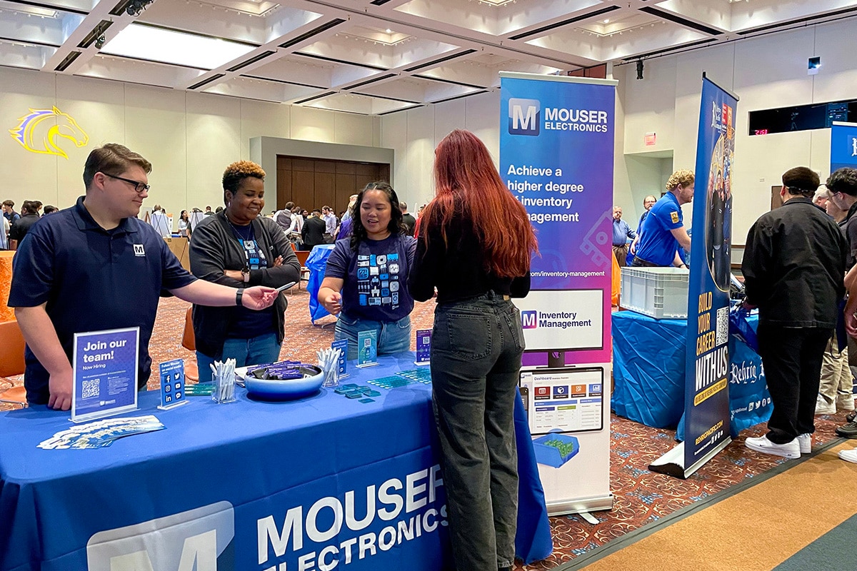 Woman standing at Mouser's booth at a UTA event, talking to three Mouser employees - opens in a new tab