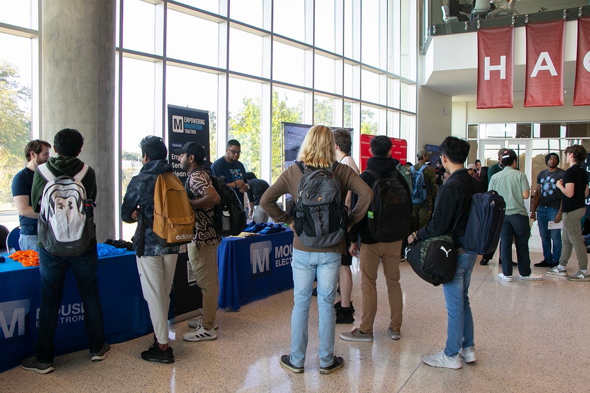 Students with backpacks gathered around Mouser tables in a large, well-lit indoor space with banners - opens in a new tab